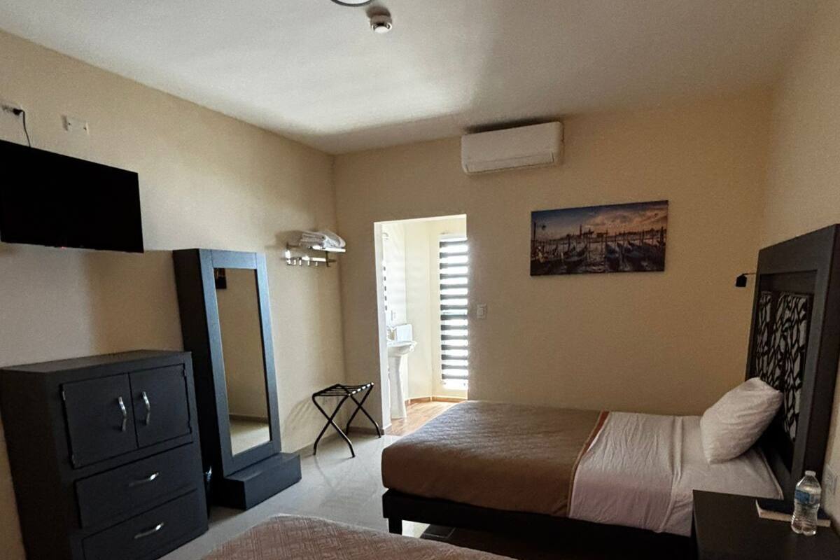 A bedroom with a bed, a dresser, a mirror, a TV, and a painting.