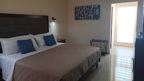 Habitación de hotel con una cama grande, cabecera, aire acondicionado instalado en la pared, un cuadro, una mesita de noche y una ventana con persianas.
