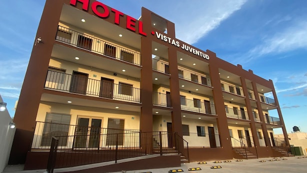 Un hotel llamado "HOTEL VISTAS JUVENTUD" con un diseño arquitectónico moderno, varios balcones y un estacionamiento con accesibilidad para personas con discapacidad.