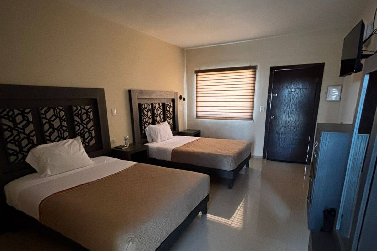 A hotel room with two beds, a desk, a television, and a door.