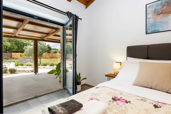 Une chambre avec un lit, une table de chevet, une lampe et une vue sur un patio extérieur.