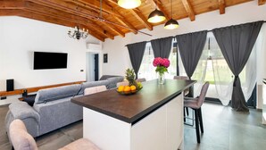 A modern kitchen with a central island, grey upholstered seating, and a dining area with a table and chairs. - LA GRONDA Holiday House (Rovinj)