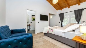 A modern bedroom with a large bed, a blue armchair, a wooden ceiling, and a TV on the wall. - LA GRONDA Holiday House (Rovinj)