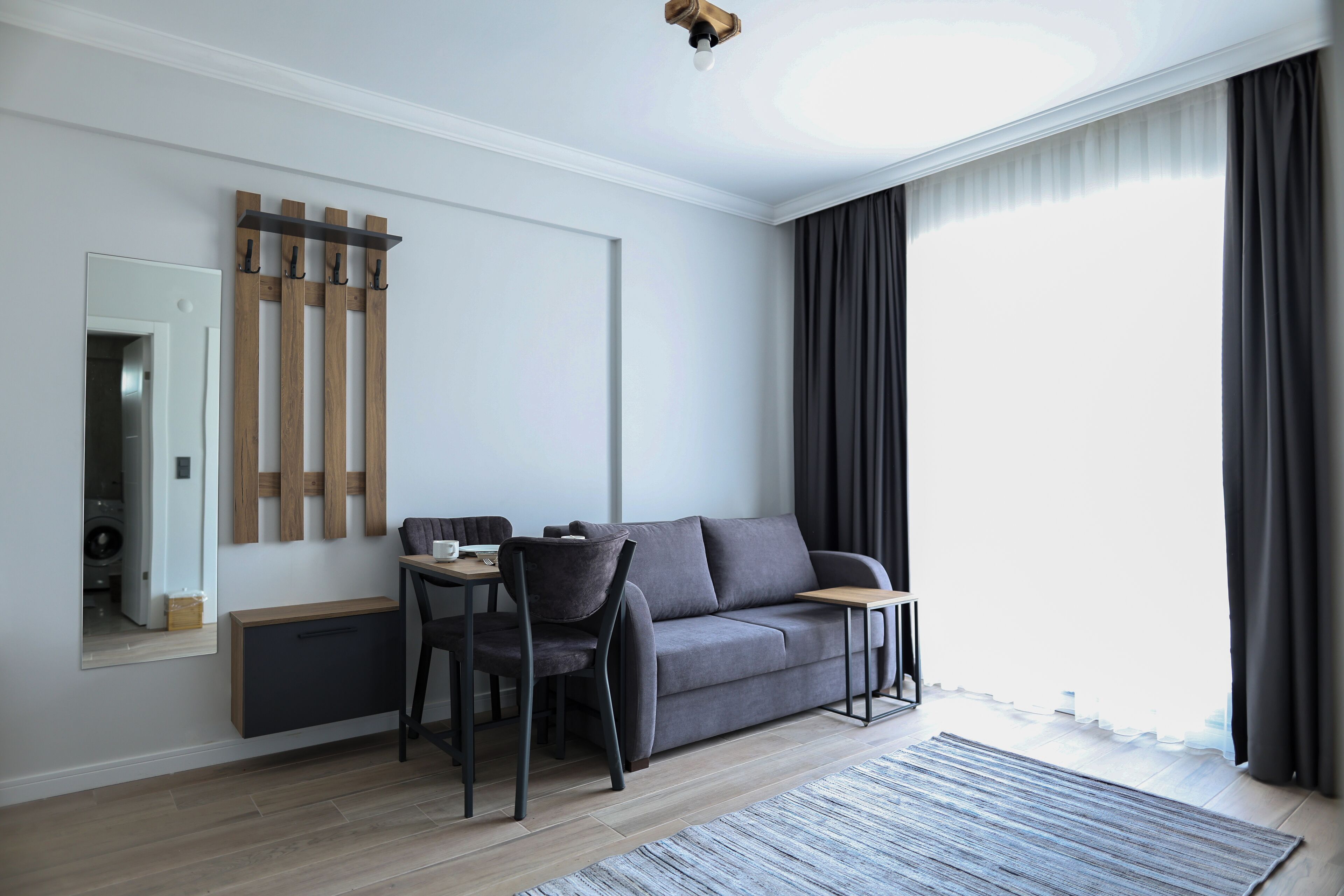 A modern living room with a grey sofa, a small table, a chair, a mirror, and a ceiling light fixture.