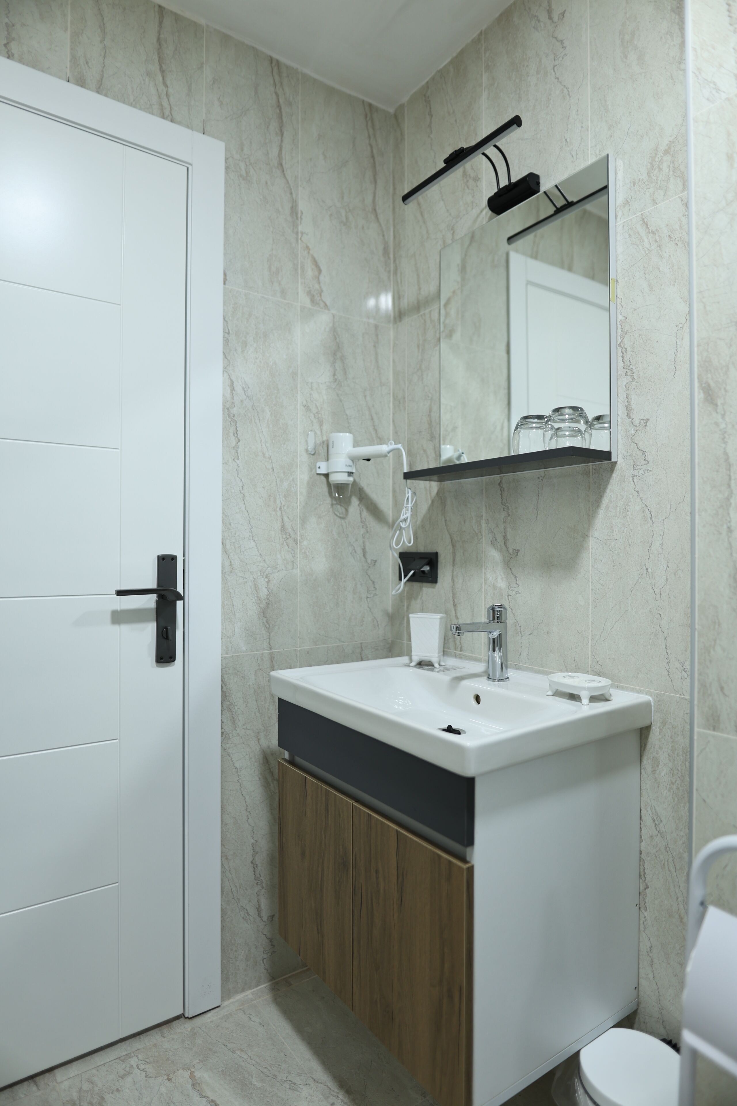 Ein Badezimmer mit weißer Tür, Waschbecken und einem Spiegel darüber sowie einer Toilette.