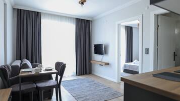 Habitació d'hotel moderna amb zona de menjador, televisió de pantalla plana penjada a la paret, taula de fusta i sofà.