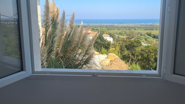 A window with a clear view of a coastal landscape, including greenery and a distant body of water. - Rent mini villa between sea and mountains... (VENTISERI)
