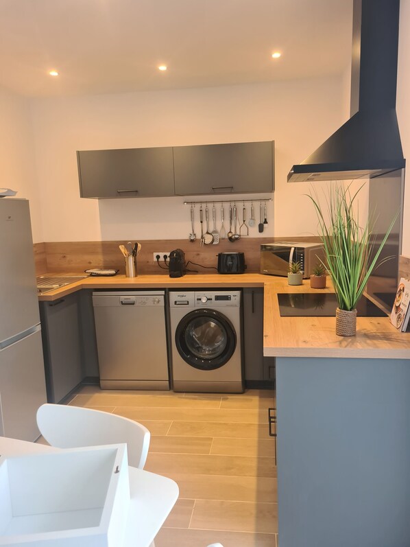 Une cuisine compacte équipée d’un lave-vaisselle, d’un lave-linge et d’appareils  électroménagers modernes.