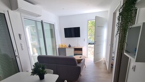 A modern living space with a dining area, a sofa, a TV mounted on the wall, and a sliding glass door leading to an outdoor area. - Rent mini villa between sea and mountains... (VENTISERI)