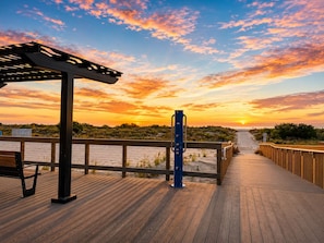 A wooden boardwalk leading to a beach with a sunset in the background. - Oceanfront Condo | NEW Retro Design | Beach + Pool (Wildwood)