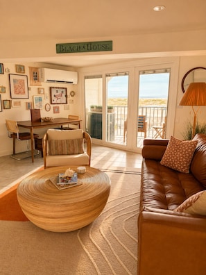 Un salon décoré sur le thème de la plage, avec un canapé, une table basse en osier et un coin repas avec des chaises.