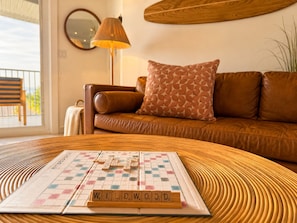 Un salon avec un jeu de Scrabble, un canapé en cuir marron, un coussin à motifs et une lampe.