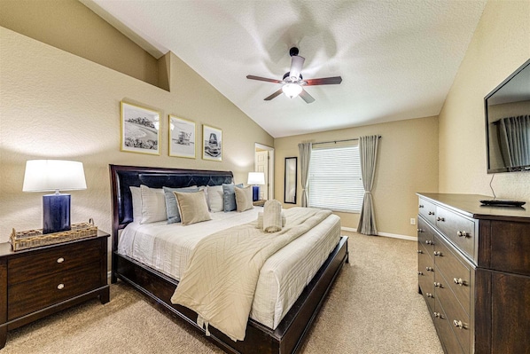 A bedroom with a bed, nightstands, a dresser, a ceiling fan, and framed pictures on the wall.