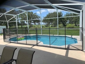 A covered swimming pool with a safety fence, lounge chairs, and a view of the surrounding landscape.