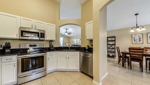 A modern kitchen with white cabinets, stainless steel appliances, and a dining area with wooden furniture. - 638 - Beautiful Pool Villa Highlands Reserve Newly Modernised 4 Bed Property (Davenport)
