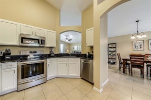 A modern kitchen with white cabinets, stainless steel appliances, and a dining area with wooden furniture.