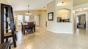A spacious living area with a dining table, chairs, a chandelier, and a kitchen area with cabinets and appliances. - 638 - Beautiful Pool Villa Highlands Reserve Newly Modernised 4 Bed Property (Davenport)