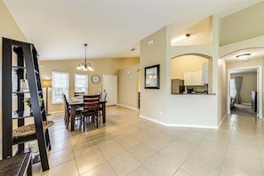 A spacious living area with a dining table, chairs, a chandelier, and a kitchen area with cabinets and appliances.