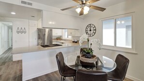 Une cuisine moderne dotée d’un îlot central, d’un coin repas avec une table en verre et d’un ventilateur de plafond.