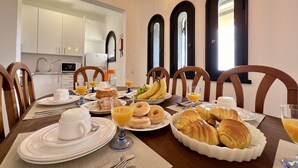 Une table de petit-déjeuner dressée avec des assiettes de croissants, des bananes et des verres de jus de fruits.