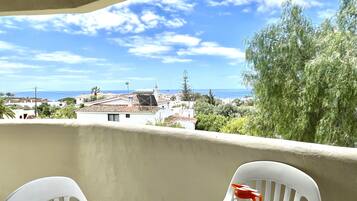 A balcony with a table and chairs, overlooking a coastal town with buildings and trees.