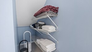 Ein Raumeck mit einer Metallregaleinheit, auf der gefaltete Handtücher und eine rote Decke liegen.