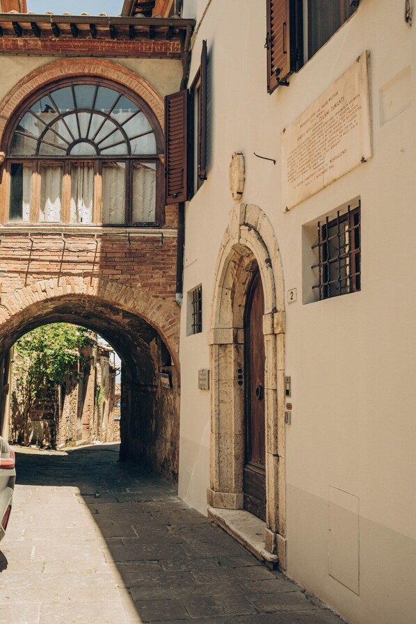 Una calle estrecha con un arco de piedra que conduce a un edificio con puerta de madera y una placa en la pared.