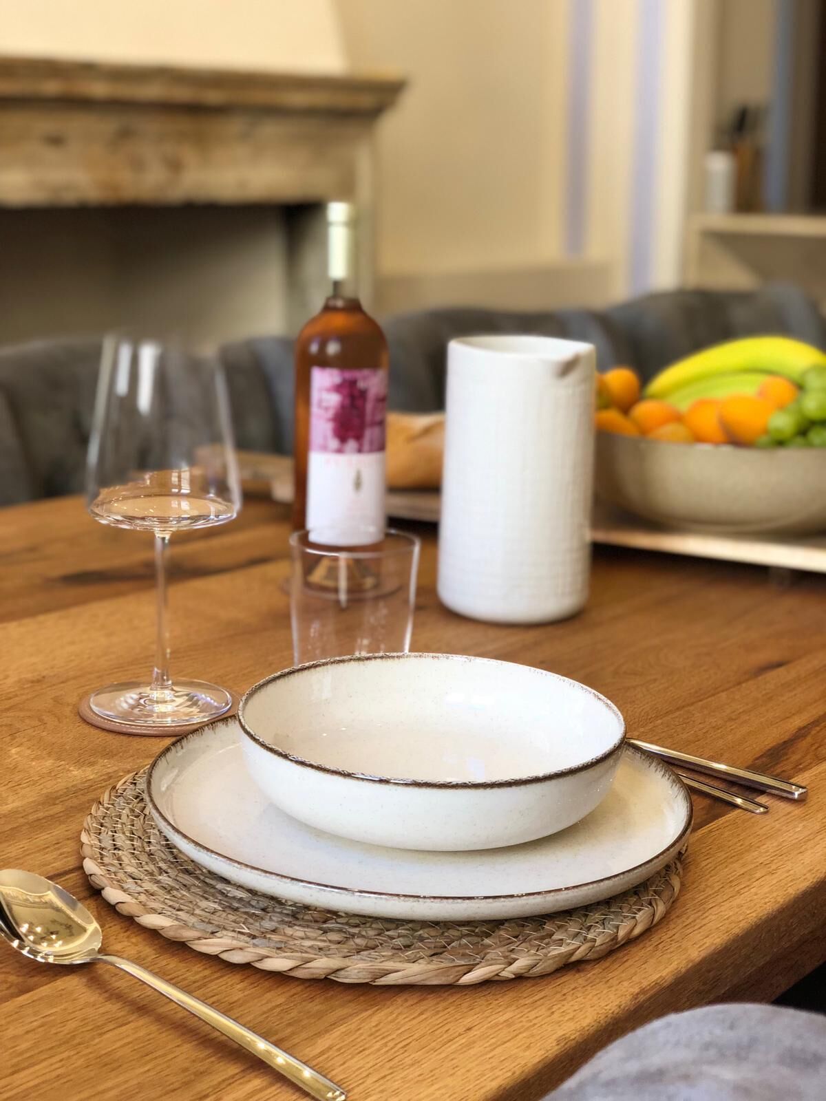 Un tavolo da pranzo con una ciotola bianca, una bottiglia di vino e due bicchieri.