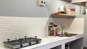 Une petite cuisine équipée d’une cuisinière à gaz, d’un évier et d’un petit plan de travail. On peut voir une poubelle et une bouteille de gaz.