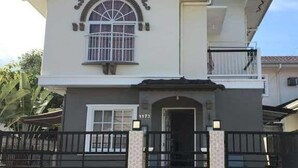 Une maison à deux étages, dotée d’une entrée fermée par un portail, d’un balcon et d’une fenêtre ornée de barreaux décoratifs.