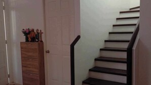 Un escalier avec une rampe, un meuble en bois doté de tiroirs et une porte surmontée d’un élément décoratif.