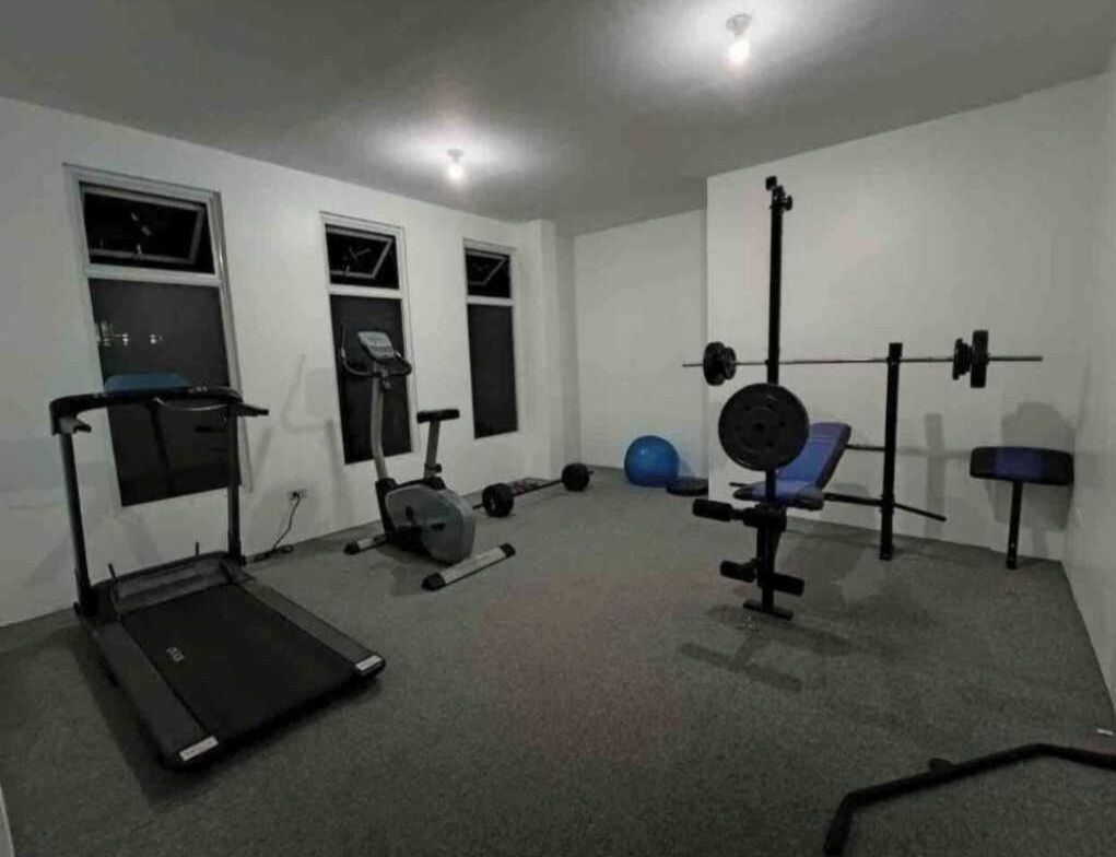 A home gym with a treadmill, stationary bike, weight bench, and various weights.