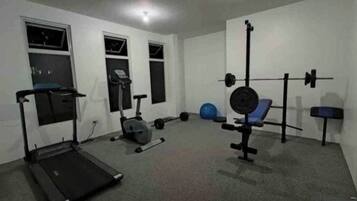 A home gym with a treadmill, stationary bike, weight bench, and various weights.