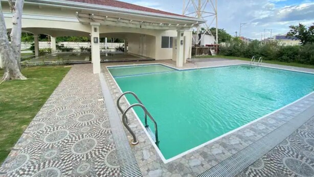 Une piscine avec une terrasse carrelée, un espace abrité et une grande tour de communication en arrière-plan.