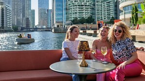 Un paisaje urbano con edificios modernos, un río y un grupo de personas sentadas en una mesa con bebidas.