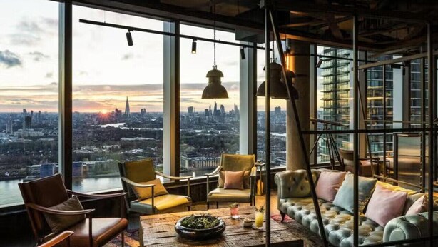 Un interior de rascacielos con vista a la ciudad, sofás de cuero, mesa de centro de madera e iluminación colgante.