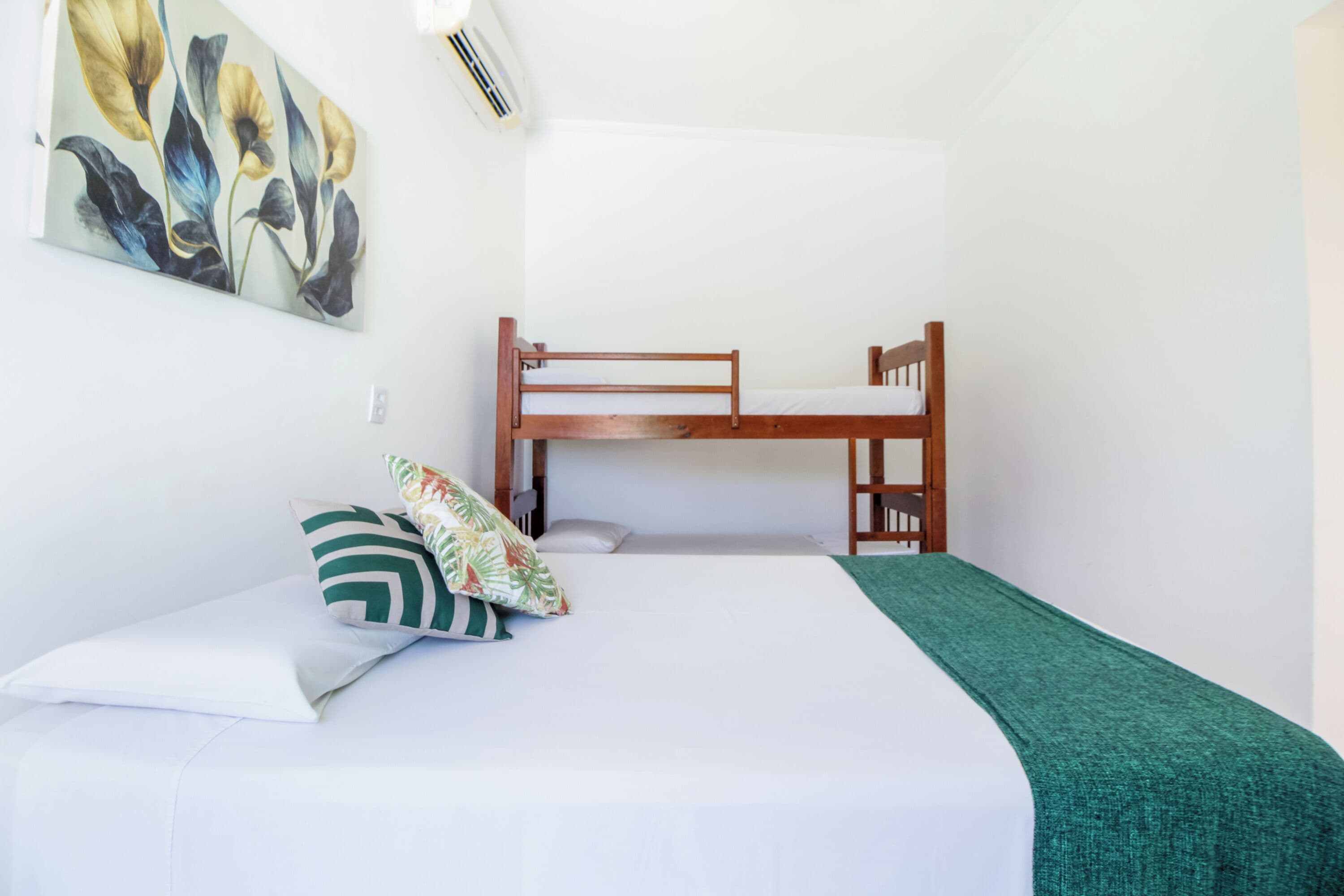 A single bed with a green blanket, a wooden headboard, and a wall-mounted air conditioner.