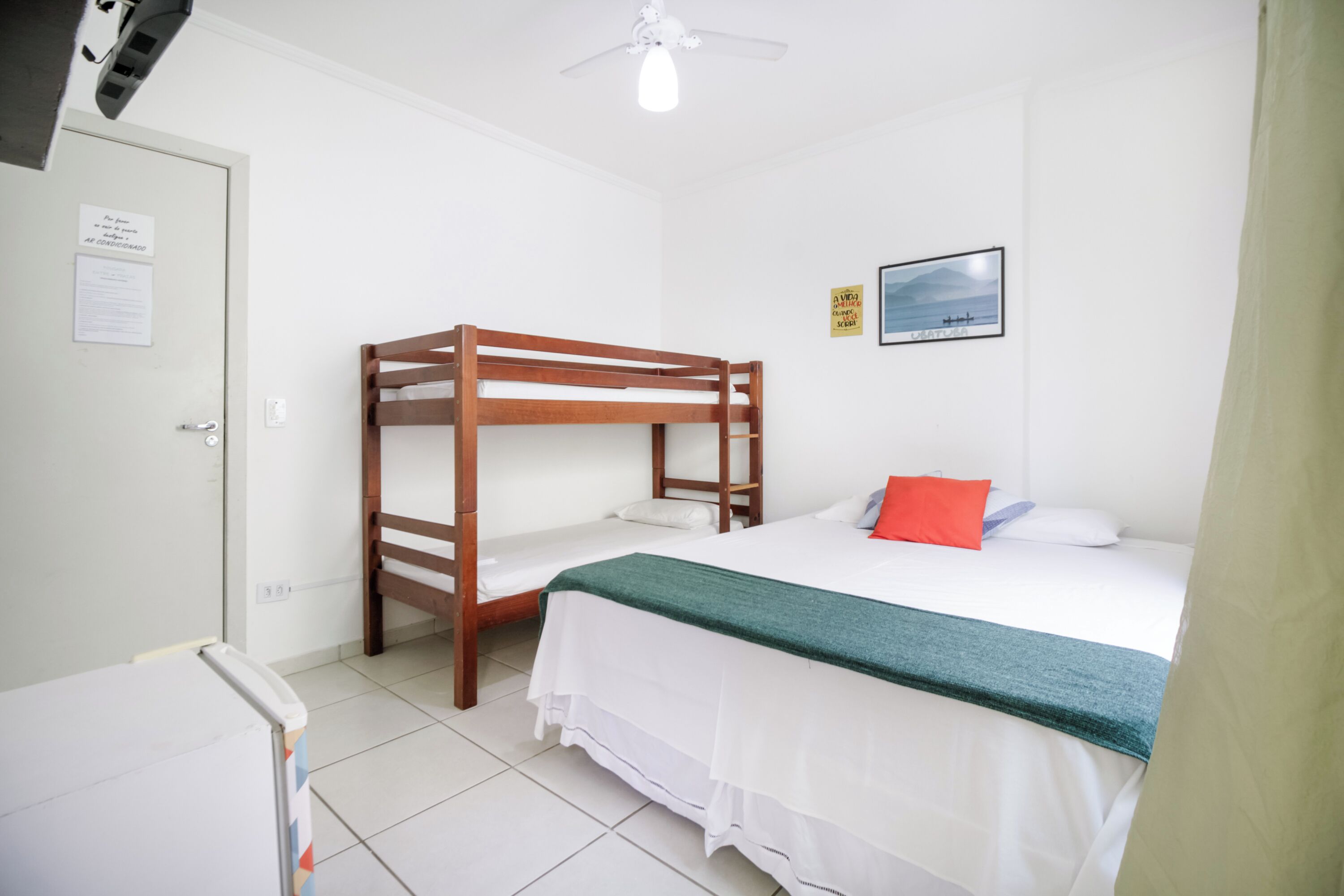 A room with a bunk bed, a desk, a chair, a bed with a green blanket, a pillow, and a framed picture on the wall.