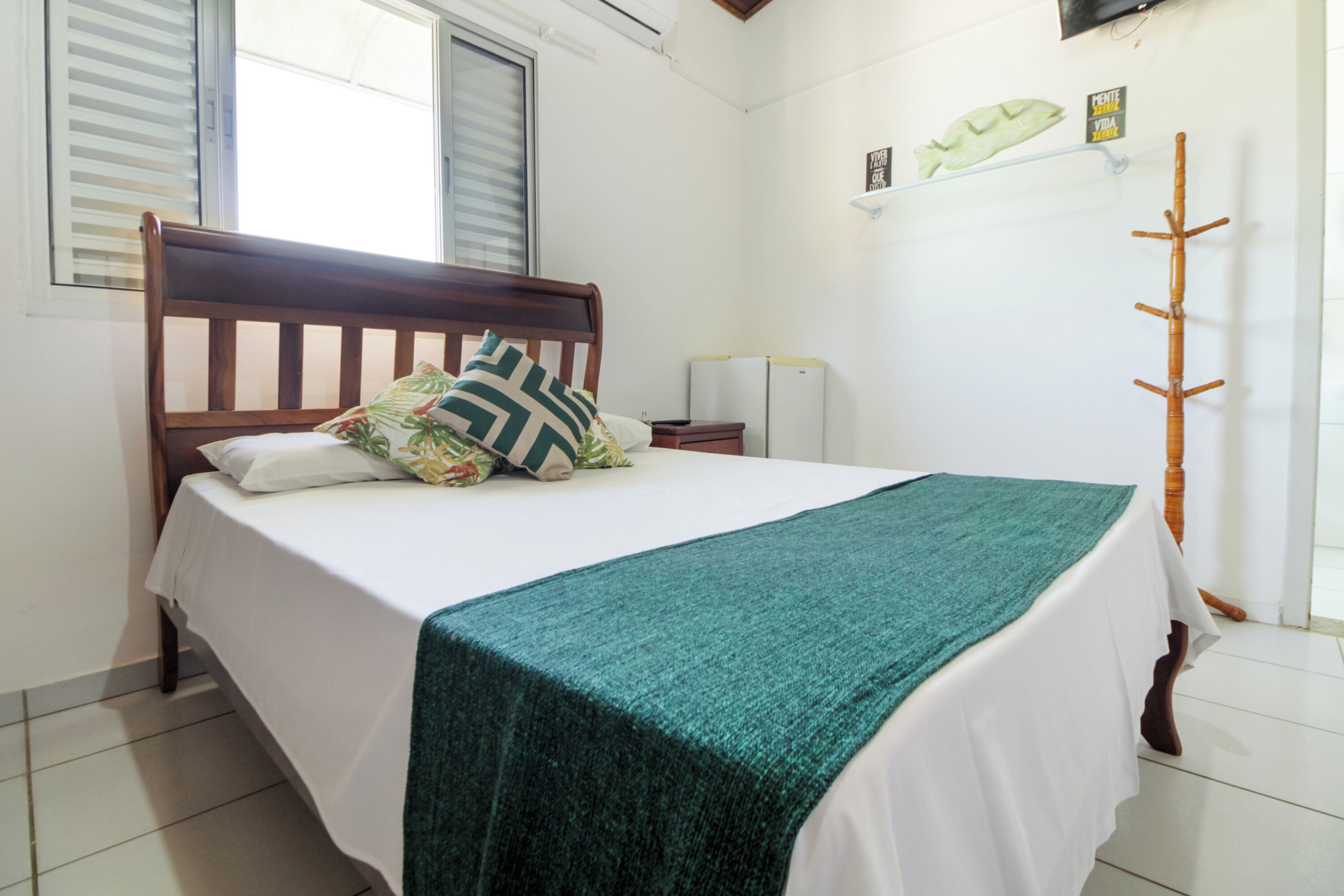 Un letto rifatto con cura, con una testiera in legno, una coperta a righe verdi e un cuscino con motivo tropicale.