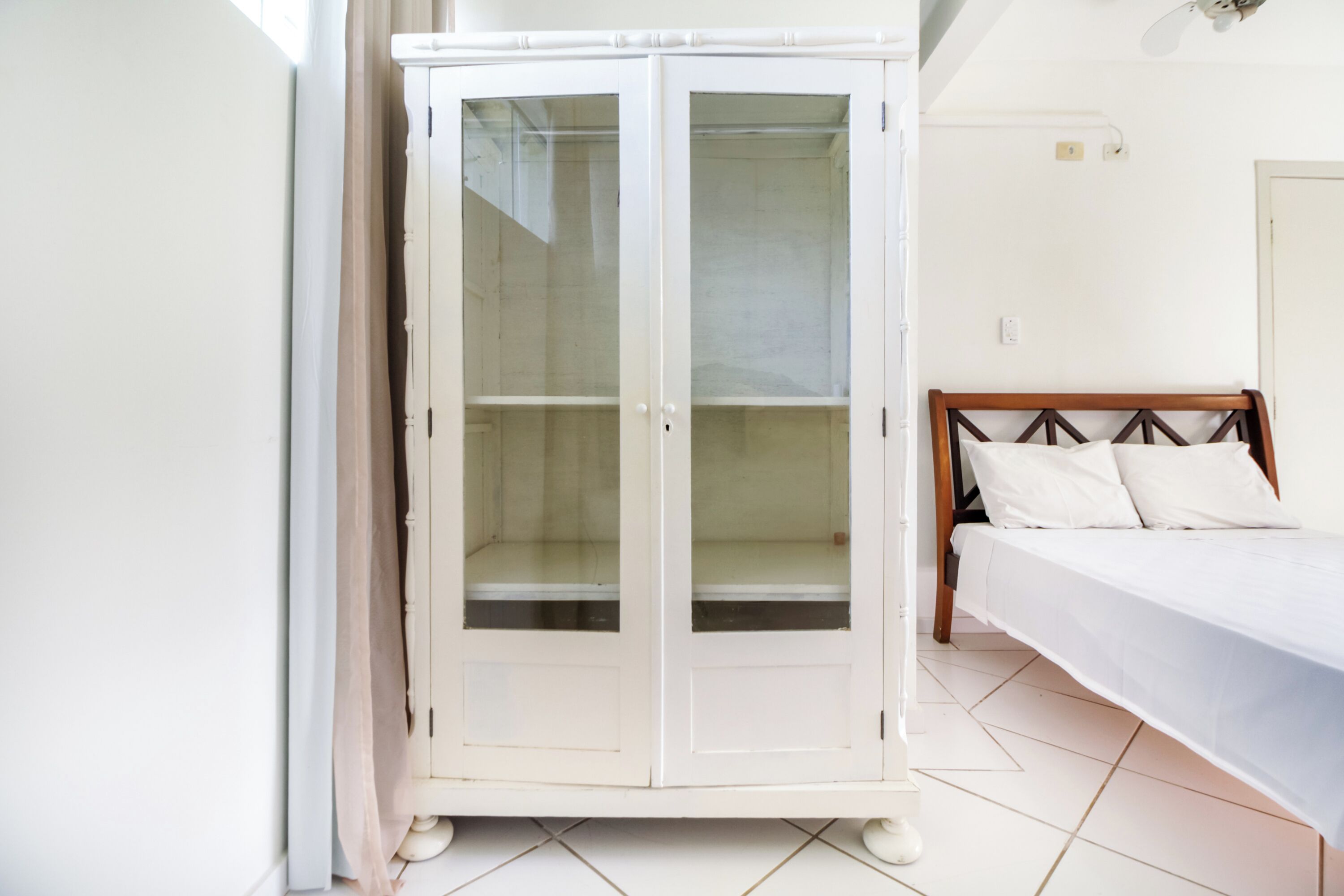 A room with a white wardrobe, a bed with wooden headboard, and a tiled floor.