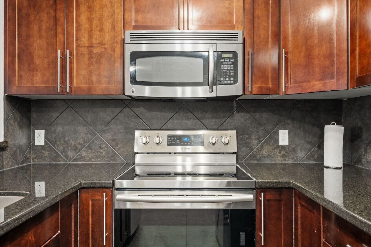 A kitchen with wooden cabinets, a stainless steel microwave, a built-in oven, and a granite countertop.