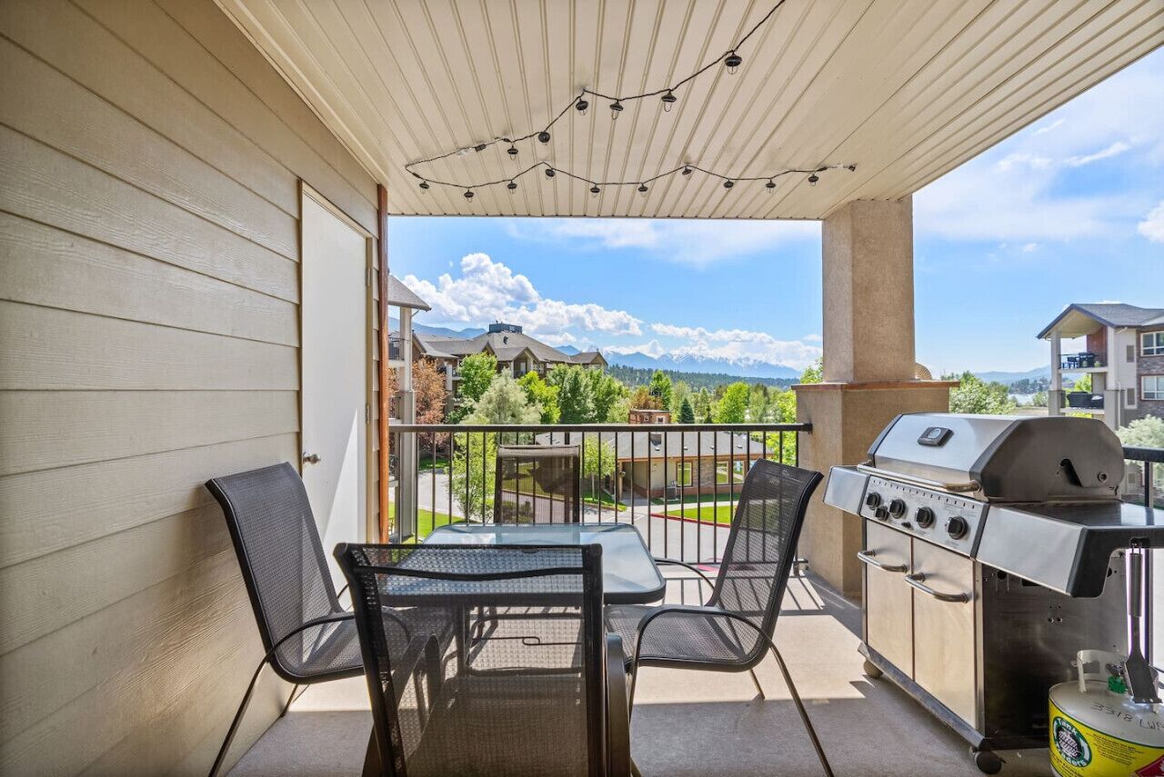 A balcony with a grill, chairs, and a table.