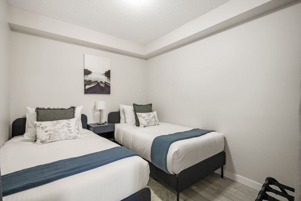 Een hotelkamer met twee bedden, een nachtkastje, een lamp en een ingelijst foto aan de muur.