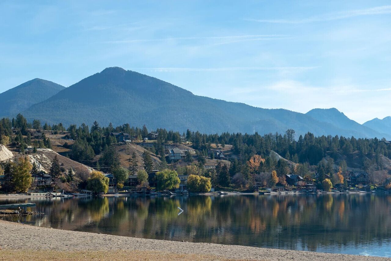 Un lac avec une montagne en arrière-plan, entouré d’arbres et de maisons.