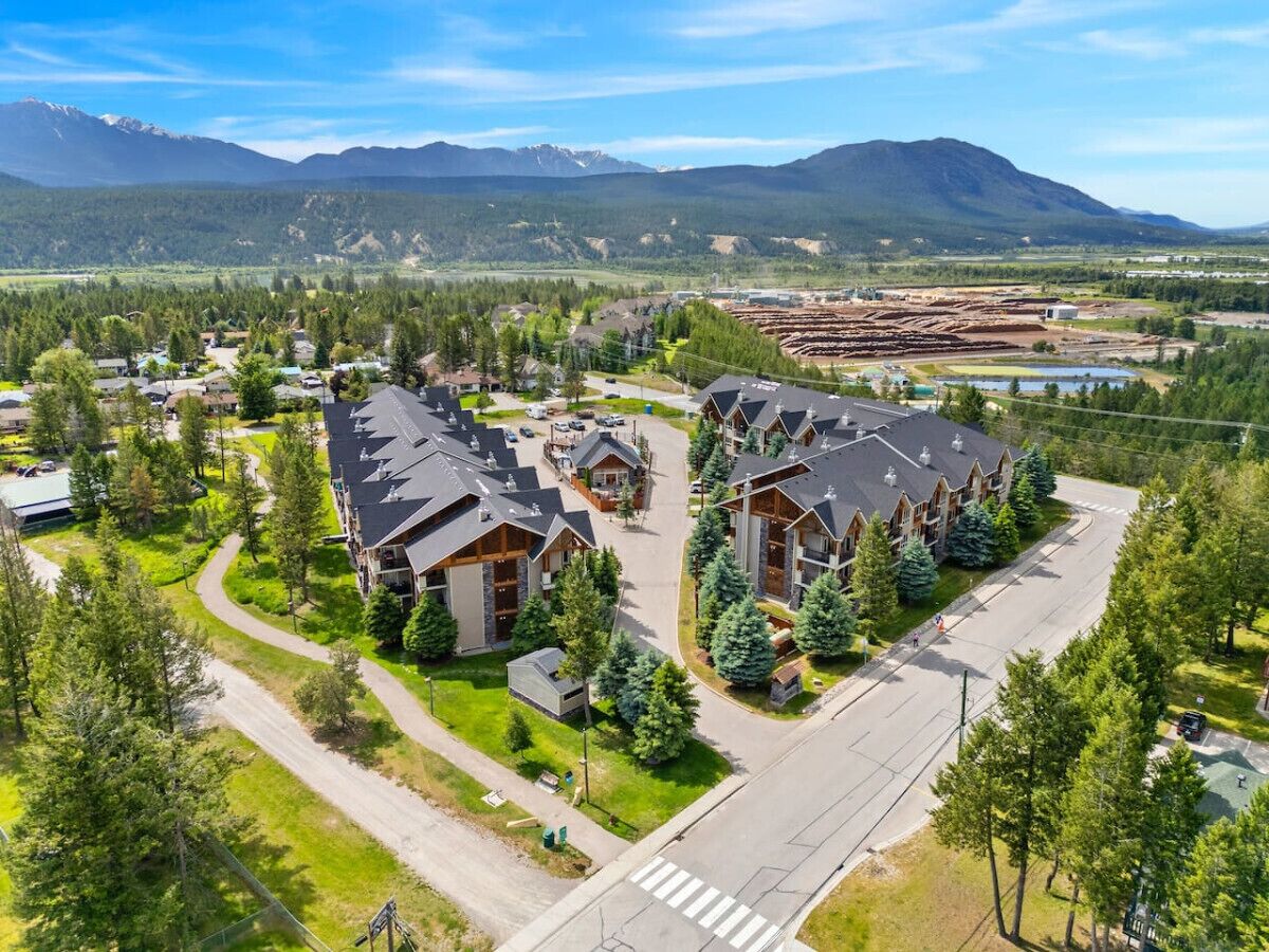 Un quartier résidentiel avec des maisons modernes, une rue principale et un paysage montagneux en arrière-plan.