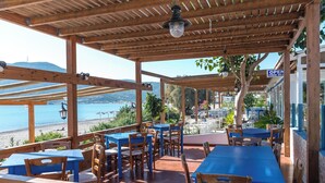 An outdoor seating area with wooden tables and chairs, overlooking a beach and the sea. - Seafront apartment in the bay of Kefalos, Kos (Kefalos)
