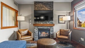 Una sala de estar con chimenea de piedra, sillones de cuero, televisor y un amplio ventanal con vistas.