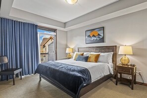 Ein Schlafzimmer mit einem Bett, zwei Nachttischen mit Lampen, einem Sessel, einem Fenster mit Vorhängen und einem Bild an der Wand.