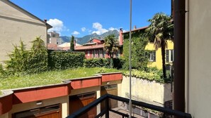 A balcony with a view of a garden, a building with a red roof, and a mountain in the background. - Center Apartment - Affitti Brevi Italia (Lecco)