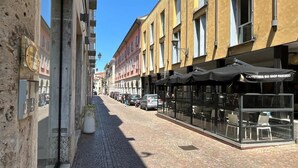 A narrow street with buildings on either side, a café with outdoor seating, and parked cars. - Center Apartment - Affitti Brevi Italia (Lecco)